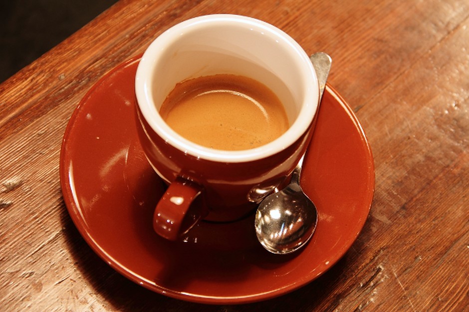 A red ceramic cup of coffee on a wooden table.